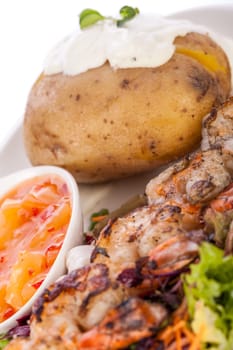 Roasted shrimp on a skewer on mixed salad with dip and foil potato prepared on a plate insulated against a white background