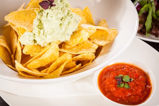 Corn chips nachos with guacamole and salsa dipp in a bowl on a plate