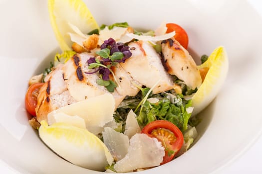 Fresh delicious caesarsalat with grilled chicken bust parmesan shards and croutons isolated against a white background