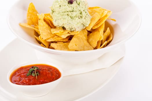Corn chips nachos with guacamole and salsa dipp in a bowl on a plate insulated against a white background