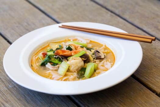 Bowl plate with freshly prepared Tom Yam soup with clanguste and coriander with chopsticks as close-up