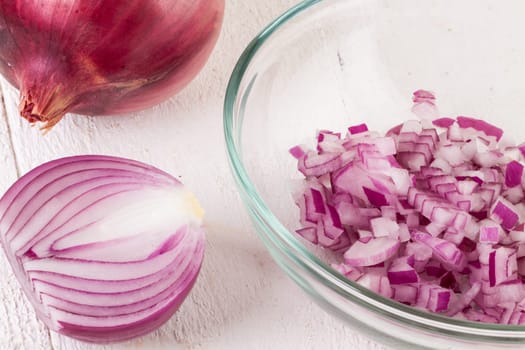Red food onion whole and in small cubes Brunoise in a bowl on a white wooden board