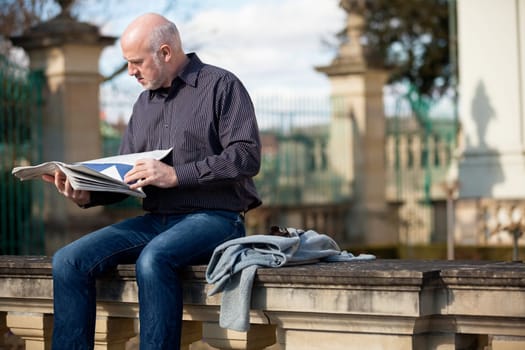 adult older man sitting outdoors reads a newspaper news free time