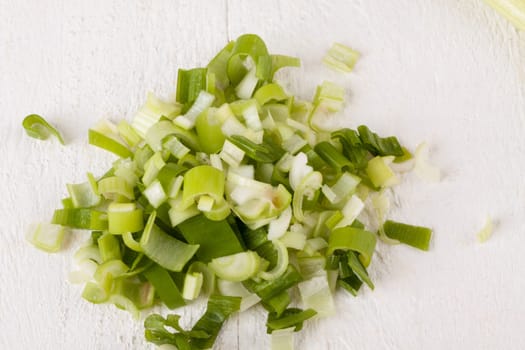 Leek spring onions with root as a whole and cut as a close-up on a white wooden board