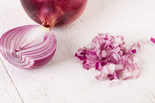 Red food onion whole and in small cubes Brunoise in a bowl on a white wooden board