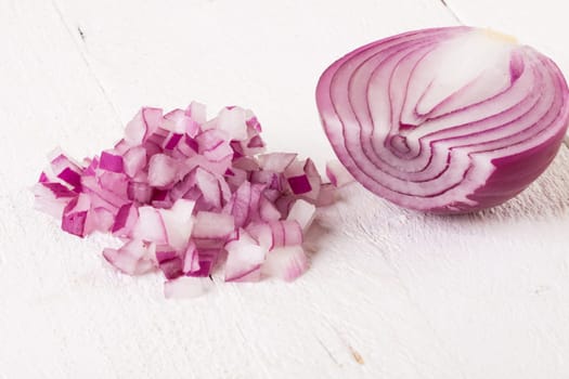 Red food onion whole and in small cubes Brunoise in a bowl on a white wooden board