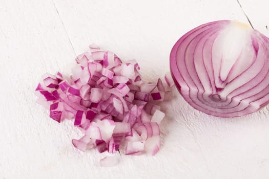 Red food onion whole and in small cubes Brunoise in a bowl on a white wooden board