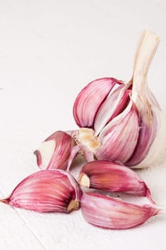 Garlic tuber with toes Fresh in whole and as a detail as a close-up on white wood