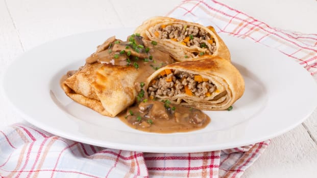 Pancake crepes tortillas stuffed with mushrooms and minced meat on a white plate close-up
