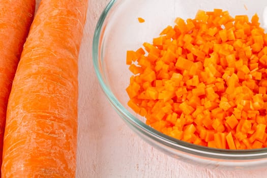 Fresh carrots beet root beet as whole and finely diced brunoise in a bowl on a white wooden board