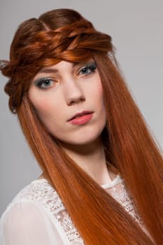Young attractive female girl with long red hair in portrait against grey background