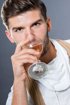 attractive young man with elegant swearing and scarf with a wine glass in his hand against a grey background