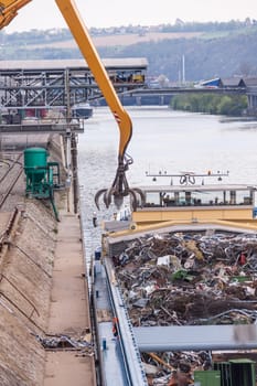 Truck crane with scrap metal loads a cargo ship at the dock with scrap