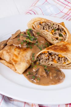 Pancake crepes tortillas stuffed with mushrooms and minced meat on a white plate close-up