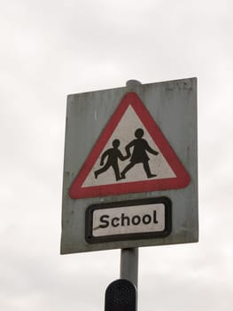 a red white and black school crossing sign with a cloudy sky background danger careful cars motor accidents careful parents and children