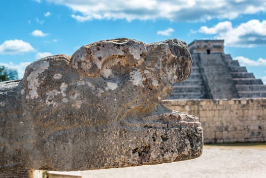 Stone snake head in Chichen Itza, Mexico with the Pyramid of Kukulcan in the background