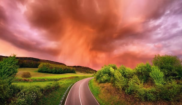 Spectacular rain clouds over a road and green landscape at sunset,with warm red light and dramatic sky