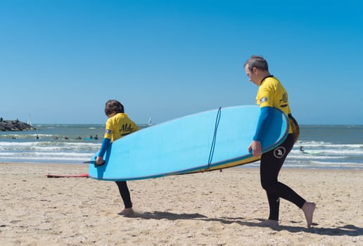 SCHEVENINGEN, NETHERLANDS - JULY 3, 2016: Two unknown surfer kids carrying a surfboard to the north sea