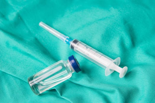 Medical syringe and vials lying on the hospital's green background. The background can be a textile part of a doctor or nurse's work uniform