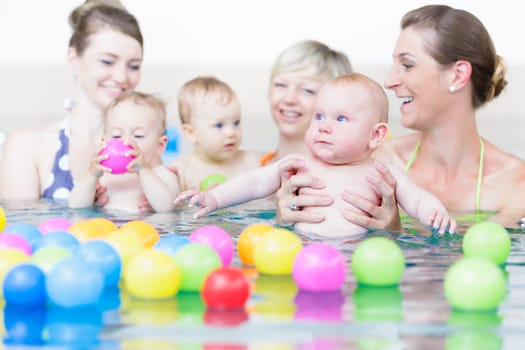 Moms and children at infant swimming lesson playing with balls