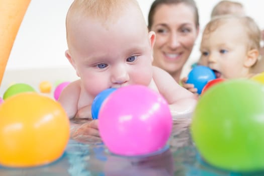 Mothers and their kids having fun at baby swimming lesson between lots of water balls