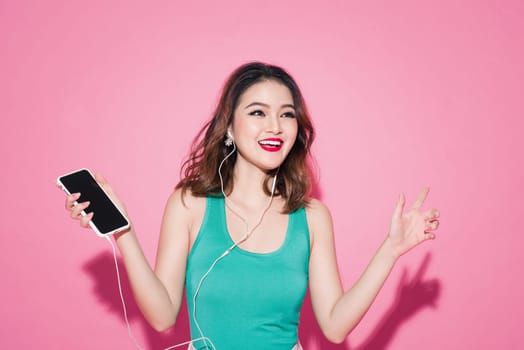 Summer lady. Beautiful asian girl with professional makeup and stylish hairstyle singing and dancing while listening to music on pink background.