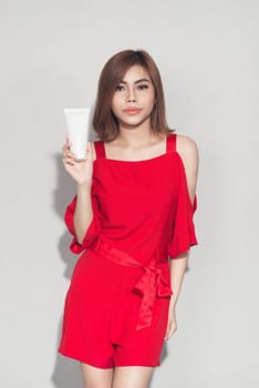 Portrait of cheerful smiling fashion girl in red dress holding cosmetic plastic tube