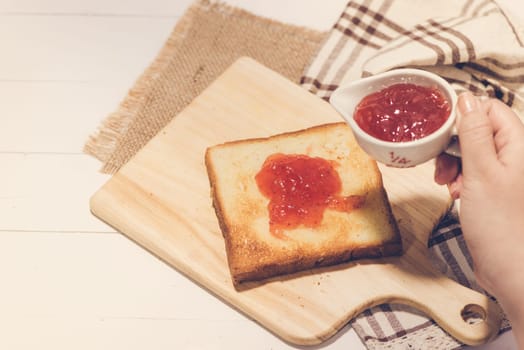 Asian woman eating bread with strawberry jam for breakfast. Focus on hands.