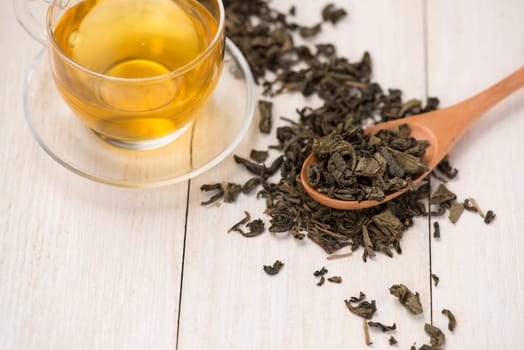 Black tea in a glass cup and tea leaves in wooden spoon on black stone background.