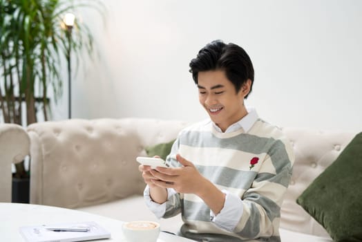 Asian male student texting by phone while sitting at the cafe shop