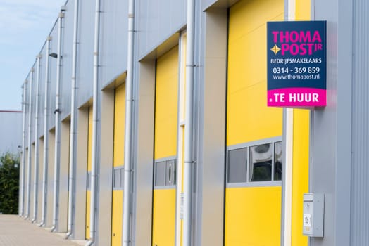 ALMELO, NETHERLANDS - JULY 9, 2016: For Rent (Te Huur) sign in front of a commercial warehouse with yellow roller doors