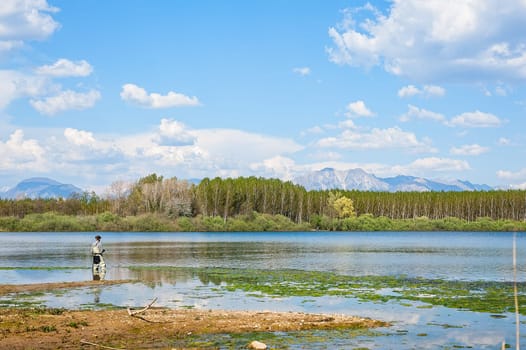 Man fishing from the shore of lake . Landscape with lake,forest,blue sky and cloud.
