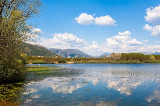 Landscape with lake,forest,blue sky and cloud.   Man fishing from the shore of lake .