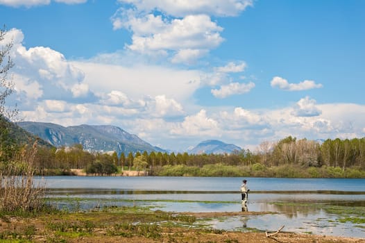 Man fishing from the shore of lake . Landscape with lake,forest,blue sky and cloud.