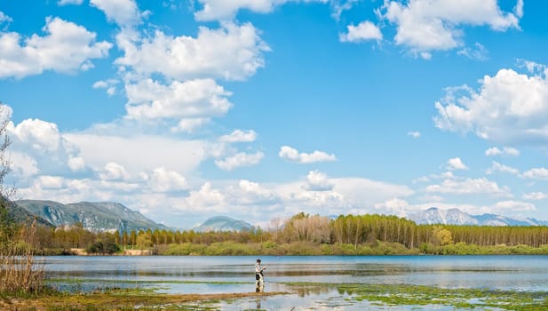 Man fishing from the shore of lake . Landscape with lake,forest,blue sky and cloud.