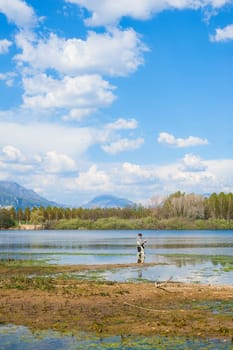 Man fishing from the shore of lake . Landscape with lake,forest,blue sky and cloud.
