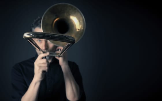 Dark portrait of a musician with a trombone, selective focus and space for text