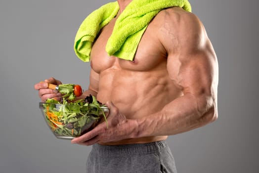 Powerful athletic man with great physique eating a healthy salad.