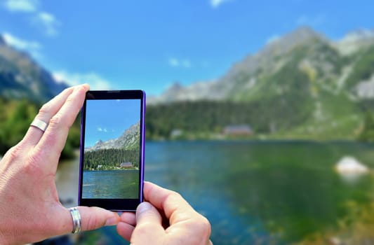 View over the mobile phone display during taking a picture of landscape in nature. Holding the mobile phone in hands and taking a photo. Focused on mobile phone screen.