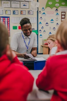 Young teacher is working with his primary school students in the classroom. He is holding a sheet of paper and is discussing it happily with the student.