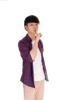 A handsome Korean teenager standing with his finger over his mouth.gesturing be quiet, isolated for white background..