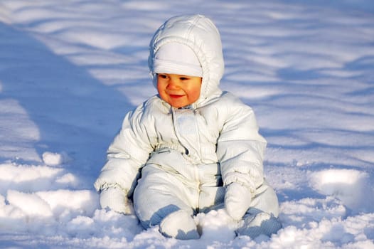 Happy smiling baby is sitting in the snow.