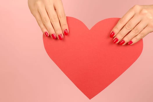 Red heart from paper in hands on red background.
