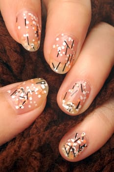 Female hand with colorful nails holds brown yarn.