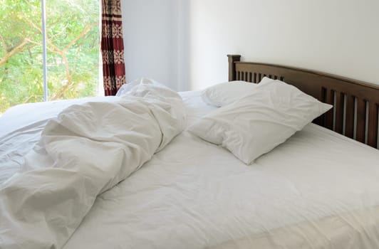 Morning view of an unmade bed in white bedroom with open curtain window