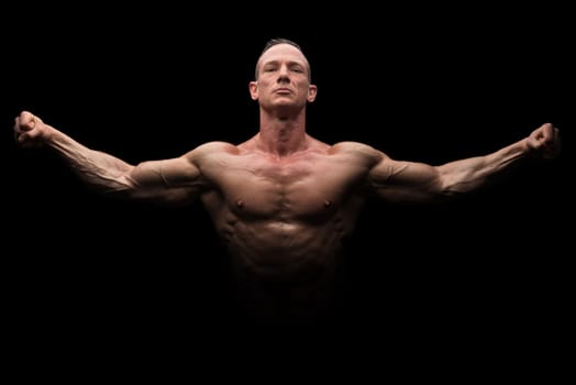 Power athletic man with open arms. Strong bodybuilder with six pack, perfect abs, shoulders, biceps, triceps and chest isolated in a black background