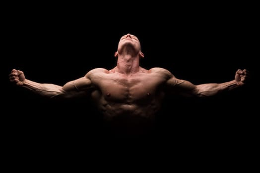 Power athletic man with open arms. Strong bodybuilder with six pack, perfect abs, shoulders, biceps, triceps and chest isolated in a black background