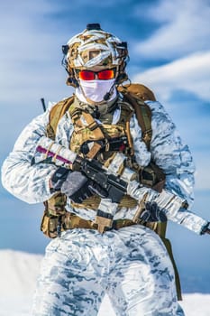 Army serviceman in winter camo somewhere in the Arctic. He wears chest rig and huge backpack, suffers from the extreme cold and strong wind, but endures while mission continues. Blue sky background