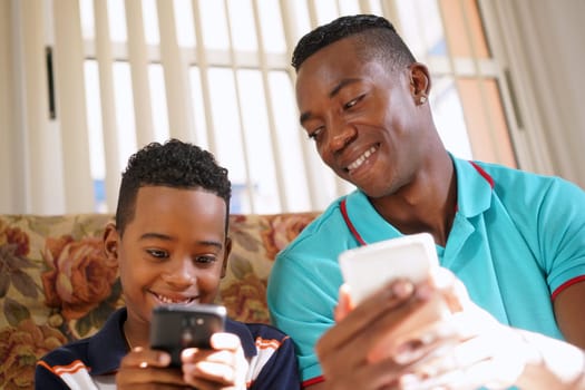 Happy black family at home. African american father and child playing game with cell phone. Hispanic dad and son having fun with smartphone.