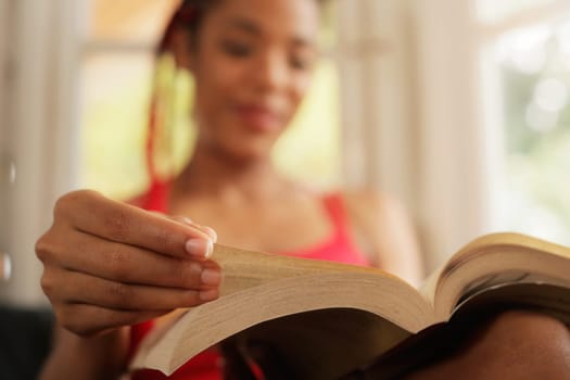 Happy female student reading book and sitting on sofa. Young african american woman relaxing, black girl lying on couch. Hispanic people and lifestyle, leisure and relaxation at home